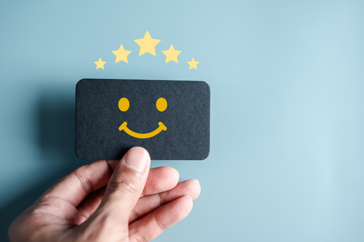 A hand holding a black card with a smiley face and stars, showing positive reviews.