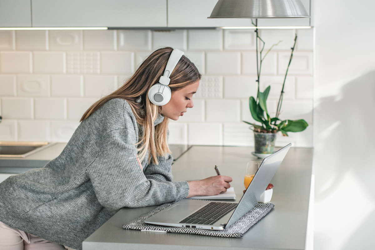 A woman wearing headphones and writing on a paper with a laptop, brainstorming new lead magnet ideas.