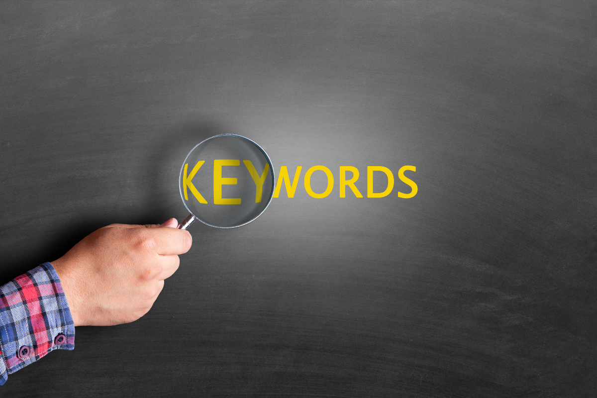 A hand holding a magnifying glass with the word "keywords" written on a black background.