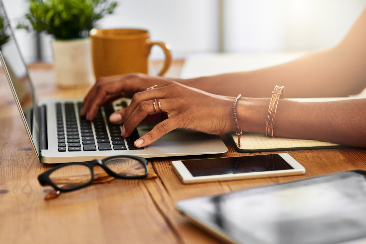 A woman typing on a laptop with a cup of coffee, working on Mailchimp.