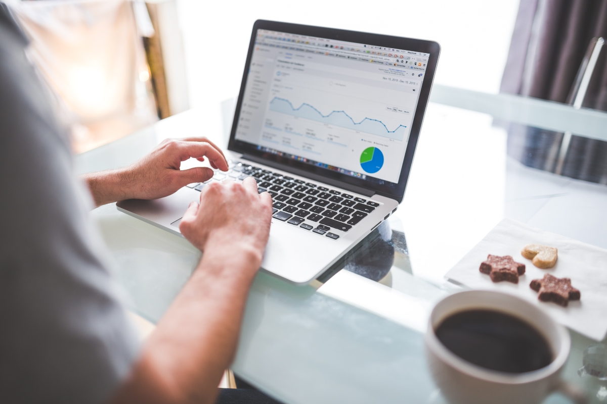 Person analyzing marketing data charts for construction companies on a laptop with a coffee cup and snacks on the side.