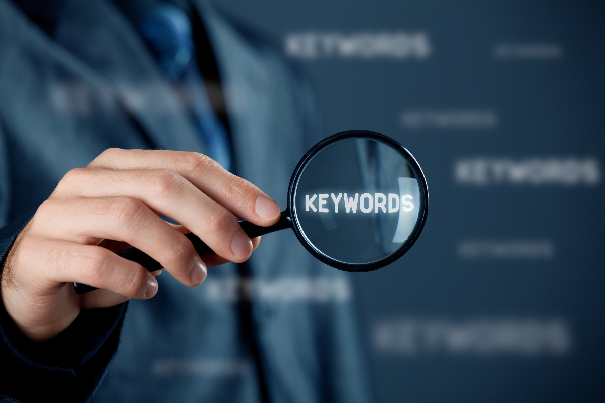 A businessman holding a magnifying glass over the word "keywords."