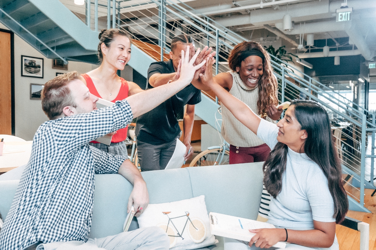 Four colleagues sharing a high-five and enjoying a moment of teamwork in a modern office setting, after successfully wrapping up an outsourced marketing project.