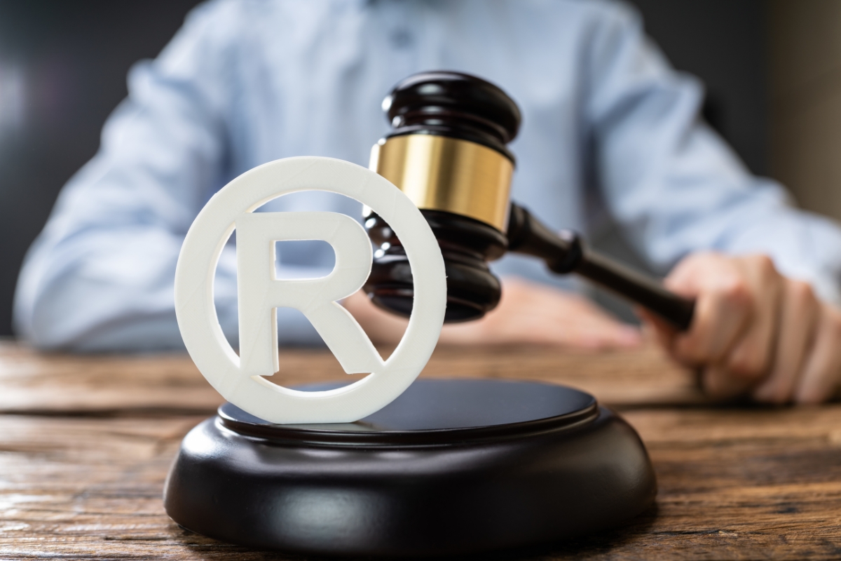 A person in a business shirt sits behind a gavel and registered trademark symbols, symbolizing legal matters related to intellectual property.