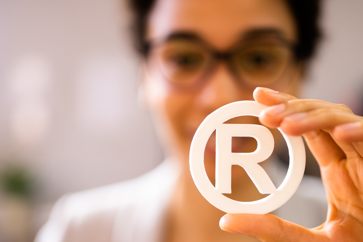 Person holding a transparent registered trademark symbol with focus on the registered trademark symbols.