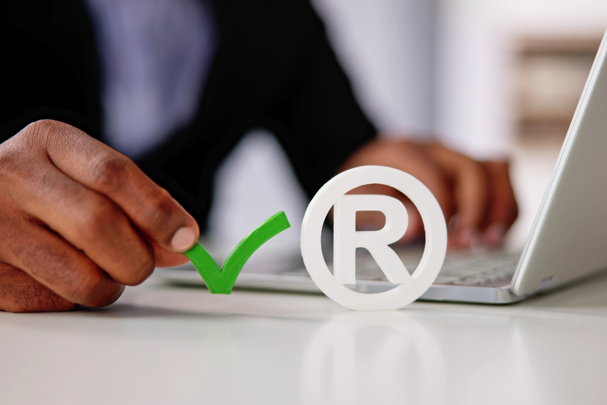 Businessperson with laptop holding a green checkmark next to white registered trademark symbols.