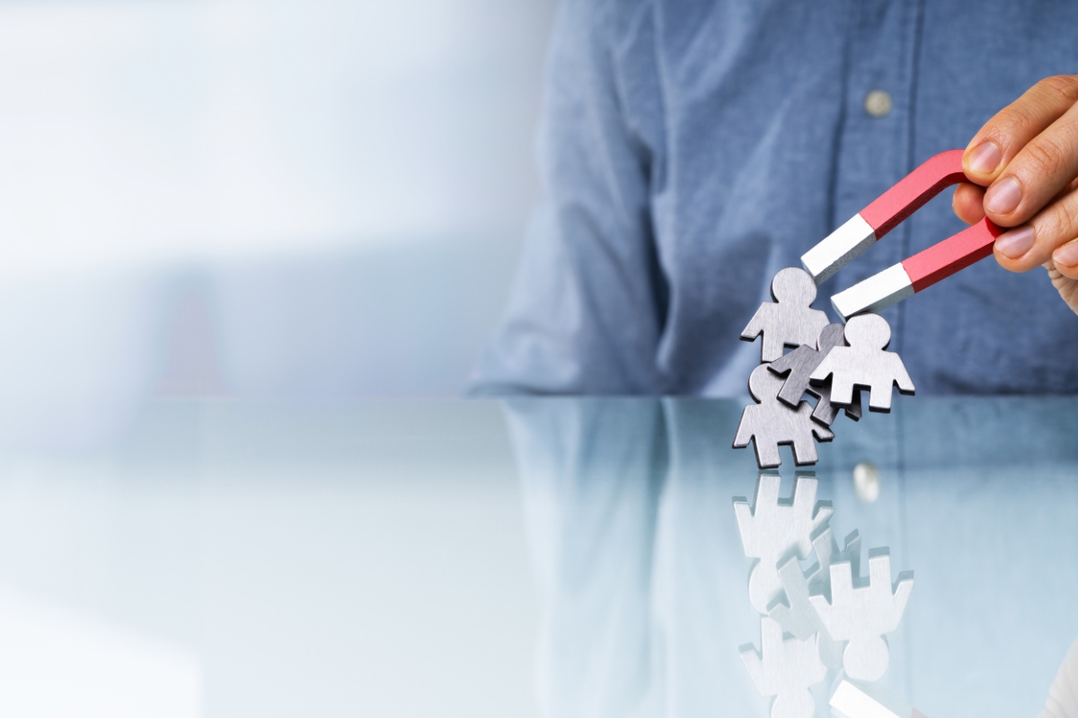 A person holding a magnet attracting paper cutout figures representing human resources or team gathering concept for service-based business marketing.