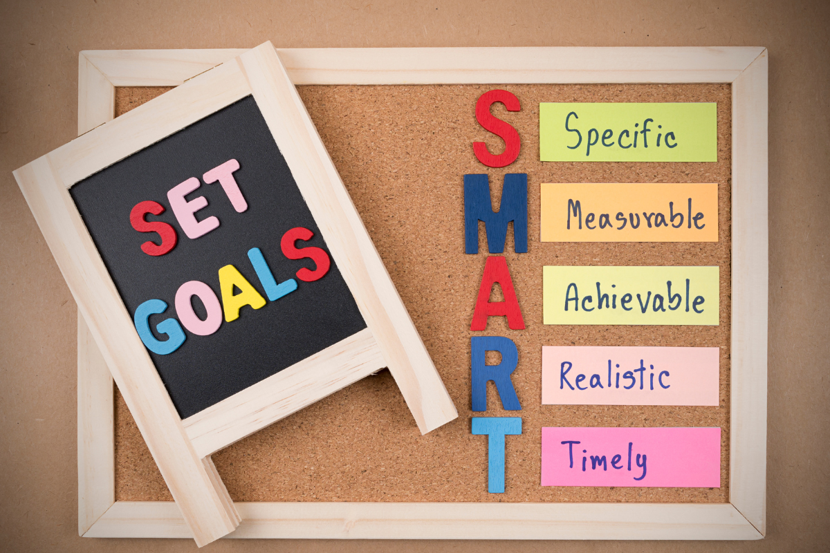 Bulletin board displaying smart goals on a blackboard and colorful sticky notes outlining the smart goals acronym: specific, measurable, achievable, realistic, and timely.