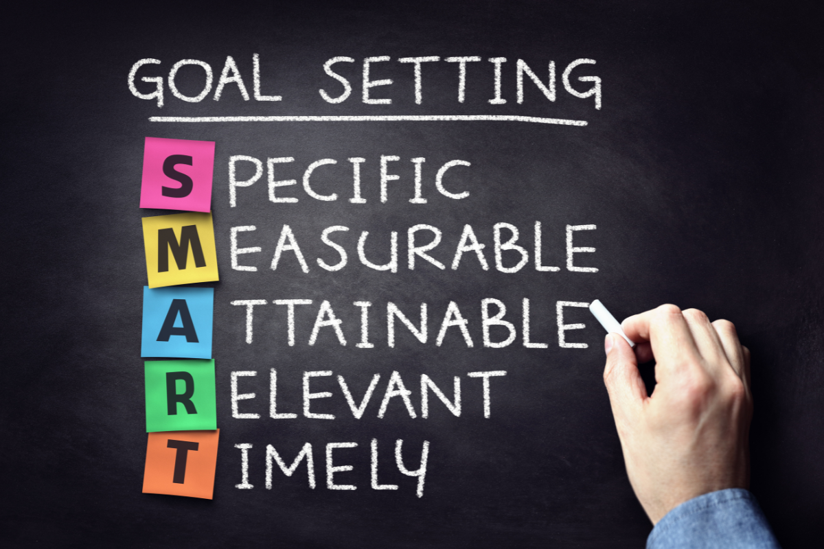 Handwriting an acronym for setting smart goals on a chalkboard with colorful block letters spelling "SMART."