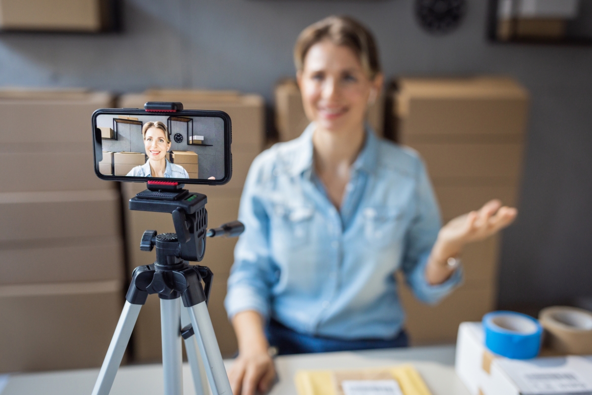 Woman recording a video blog for social media engagement while sitting at a desk with shipping materials.