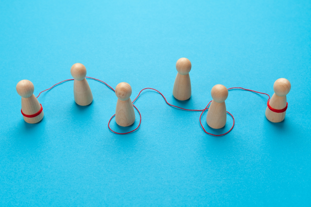 Wooden figures connected by a red thread on a blue background symbolizing word of mouth marketing.