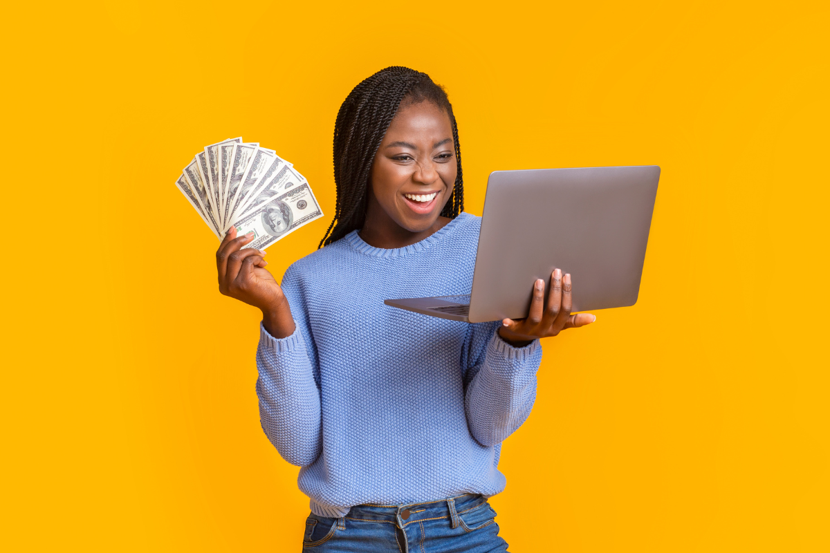 A woman holding money and a laptop on a yellow background.