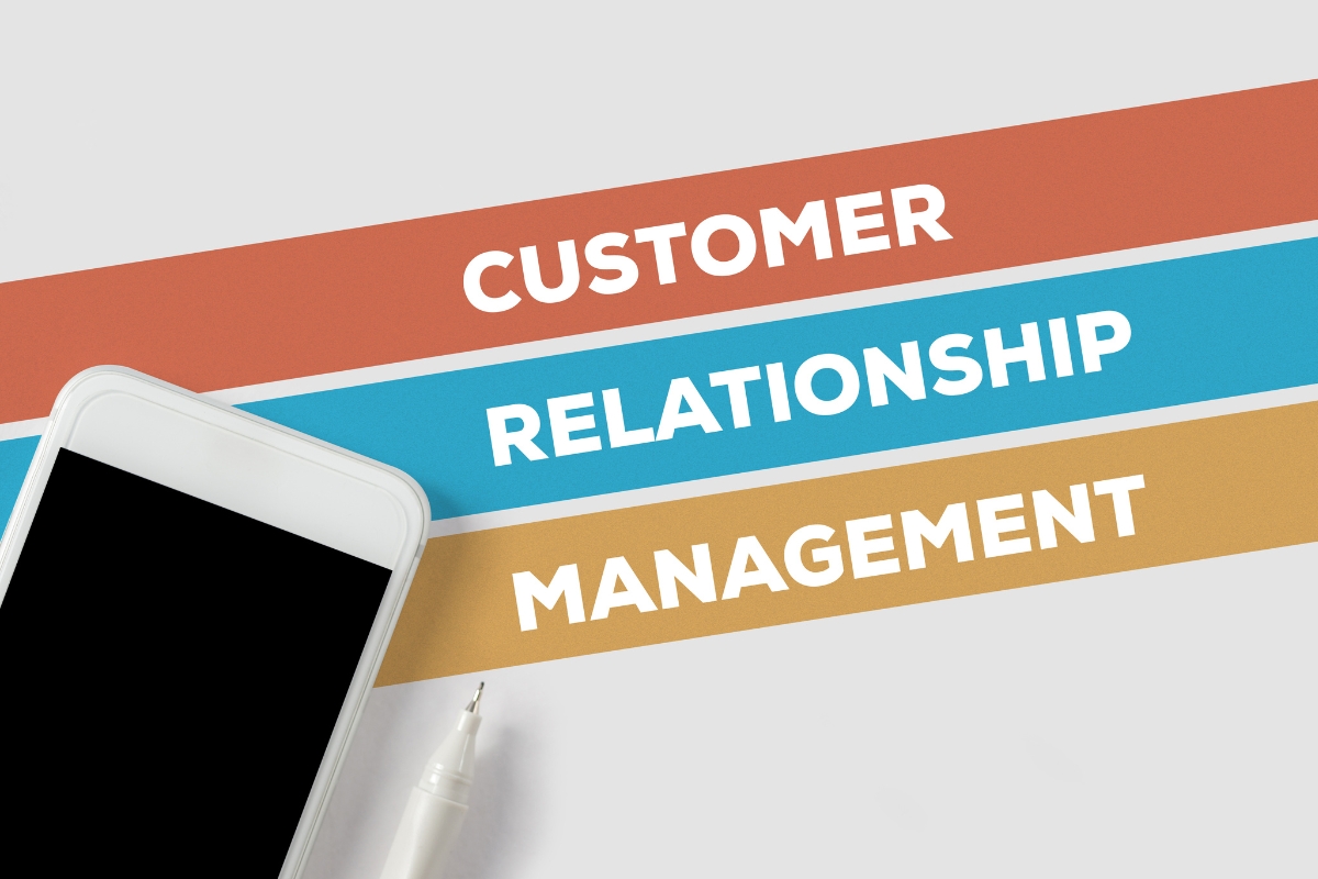 Smartphone and pen next to colorful bars with text "customer relationship management" on a pristine background.