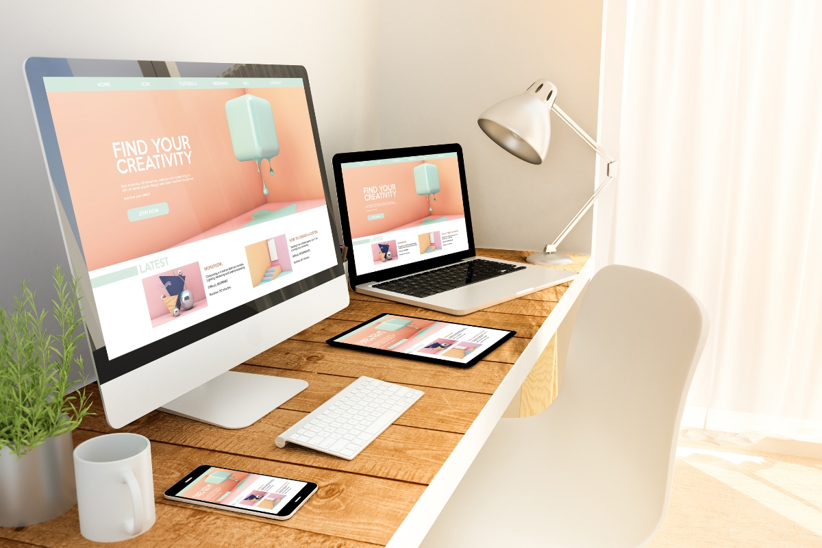 A modern workspace featuring a desktop, laptop, tablet, and smartphone all displaying a coordinated "find your creativity" website built with Elementor in WordPress, with a white desk lamp and a coffee cup.