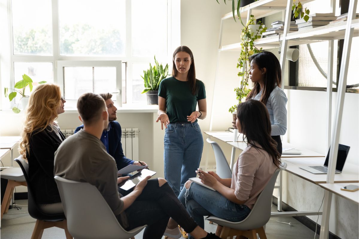 A woman presenting strategies for employee advocacy on social media to a diverse group of colleagues in a bright, modern office setting.