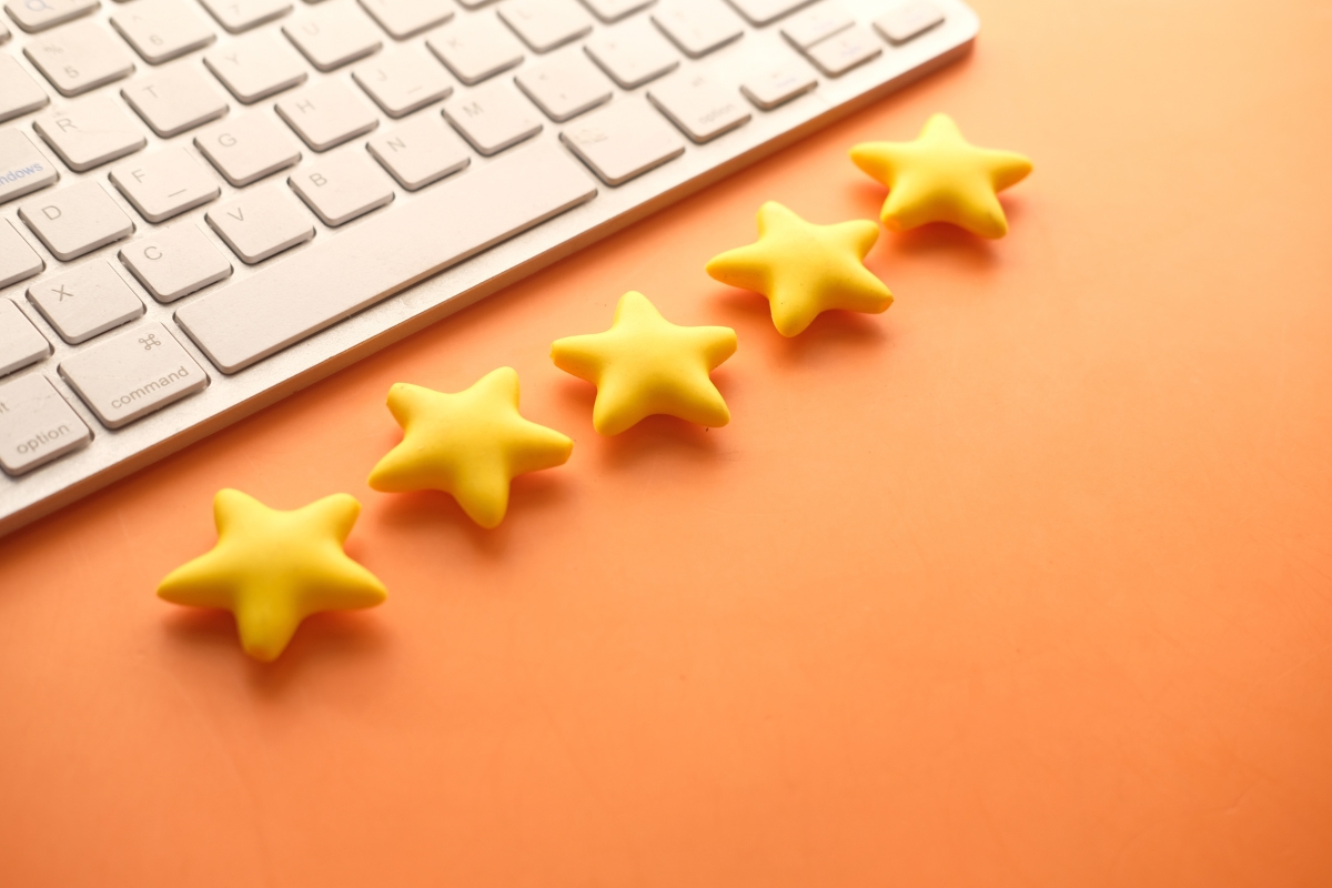 Five yellow star-shaped figures, symbolizing Google reviews, arranged in a line on a peach background next to a white keyboard.