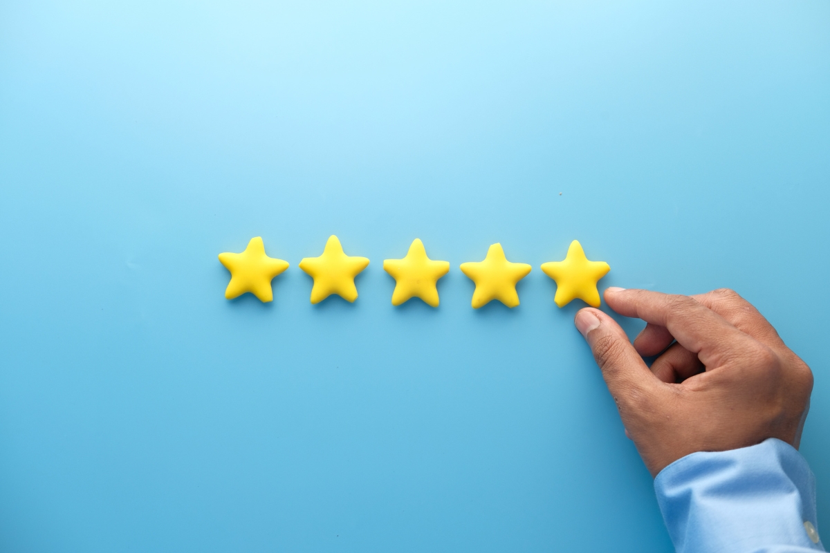 A hand placing the fifth yellow star in a row against a blue background, symbolizing a five-star Google reviews rating.