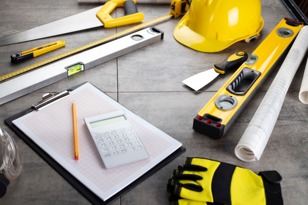 Construction tools and houzz pro safety gear, including a helmet, gloves, calculator, and measuring instruments on a gray surface.