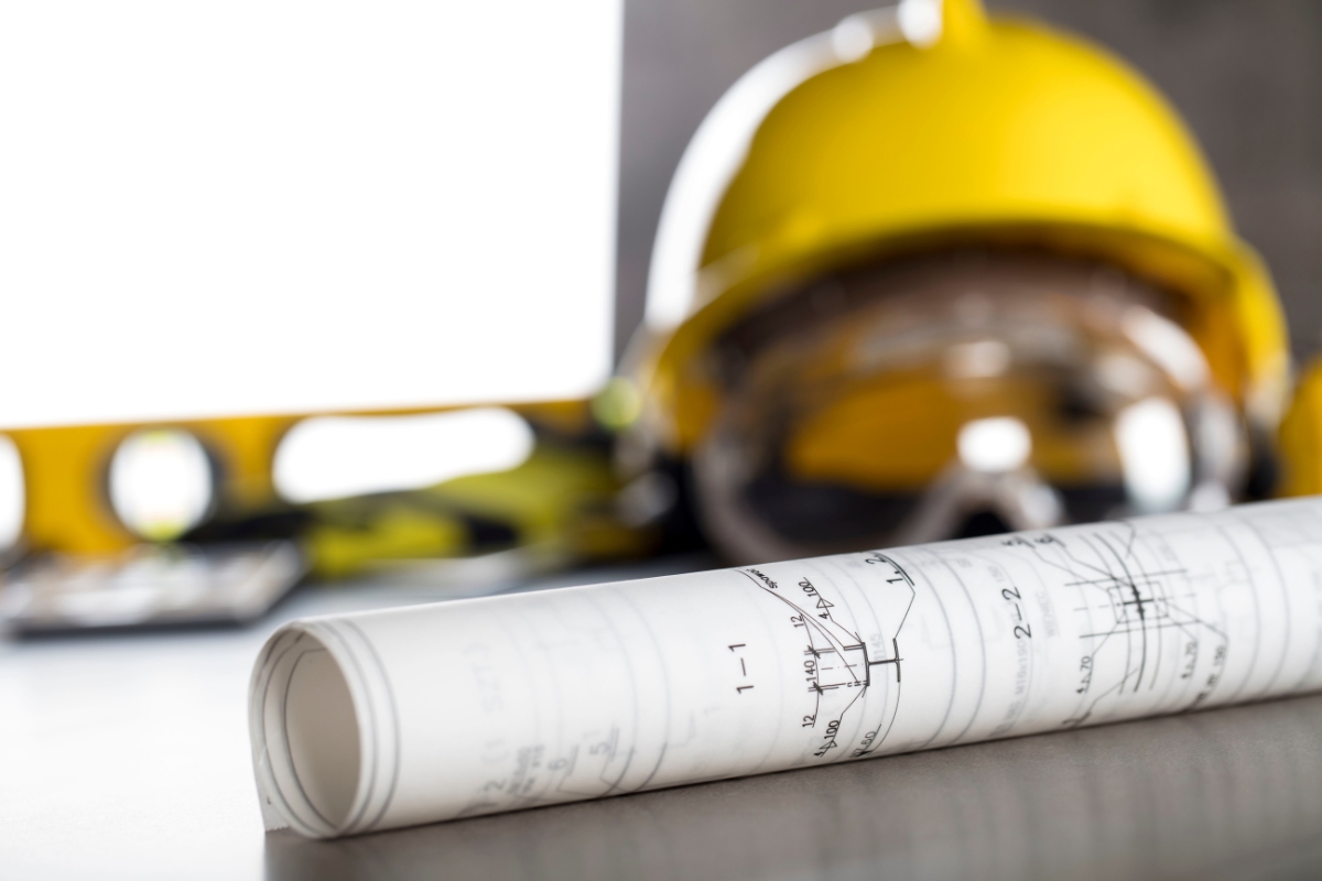 Yellow safety helmet and goggles on a table with rolled-up architectural blueprints in the foreground, ideal for houzz pro users.