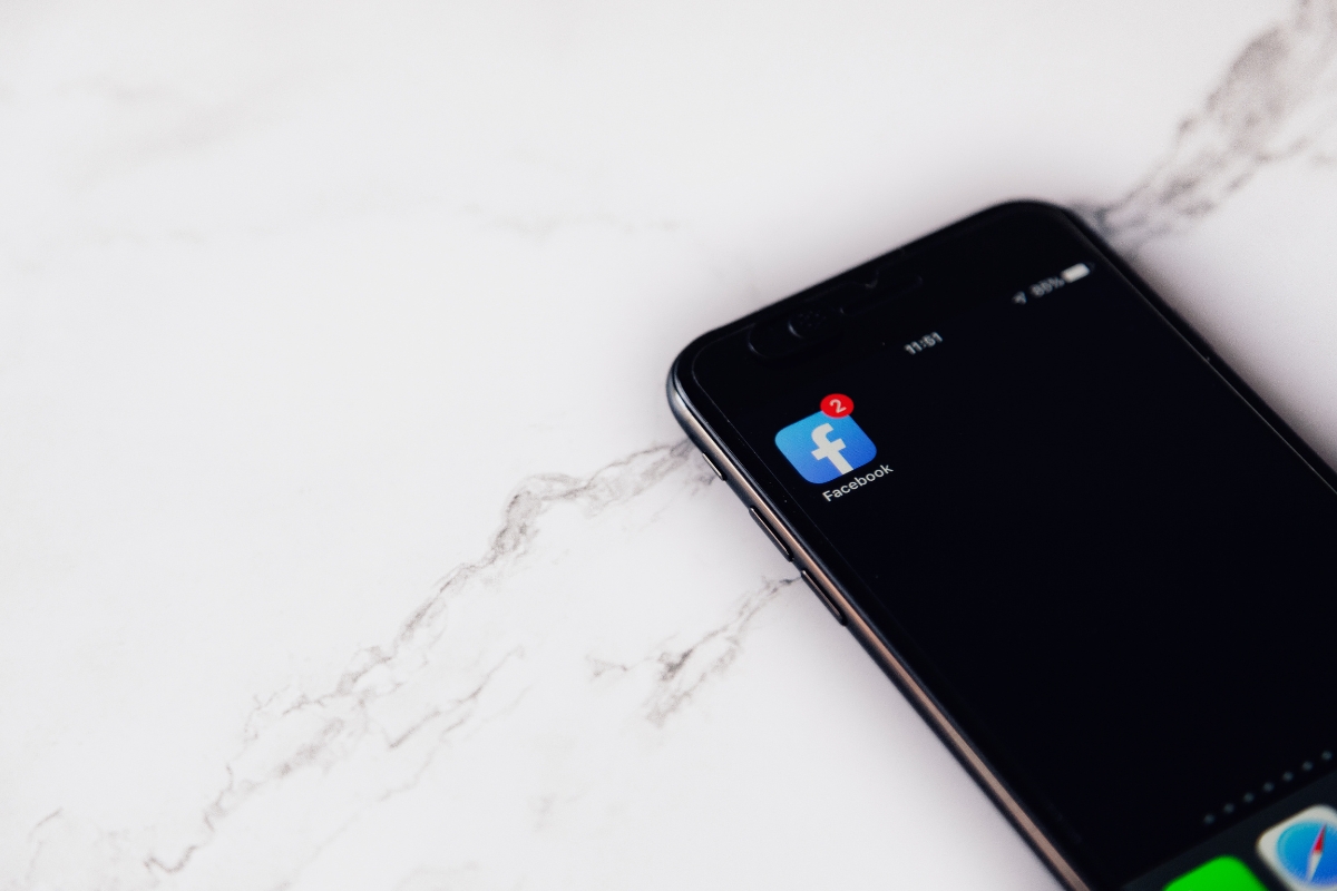 Black smartphone displaying a "how to improve your facebook business page" notification with one message on screen, resting on a white marble surface.