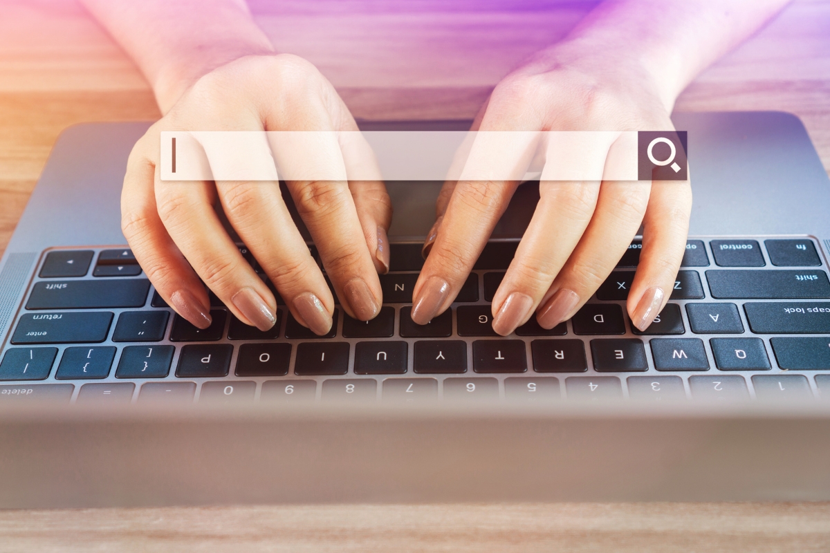 Two hands typing on a laptop keyboard, with a digital search bar graphic overlaying the image, demonstrating how to search on a website.