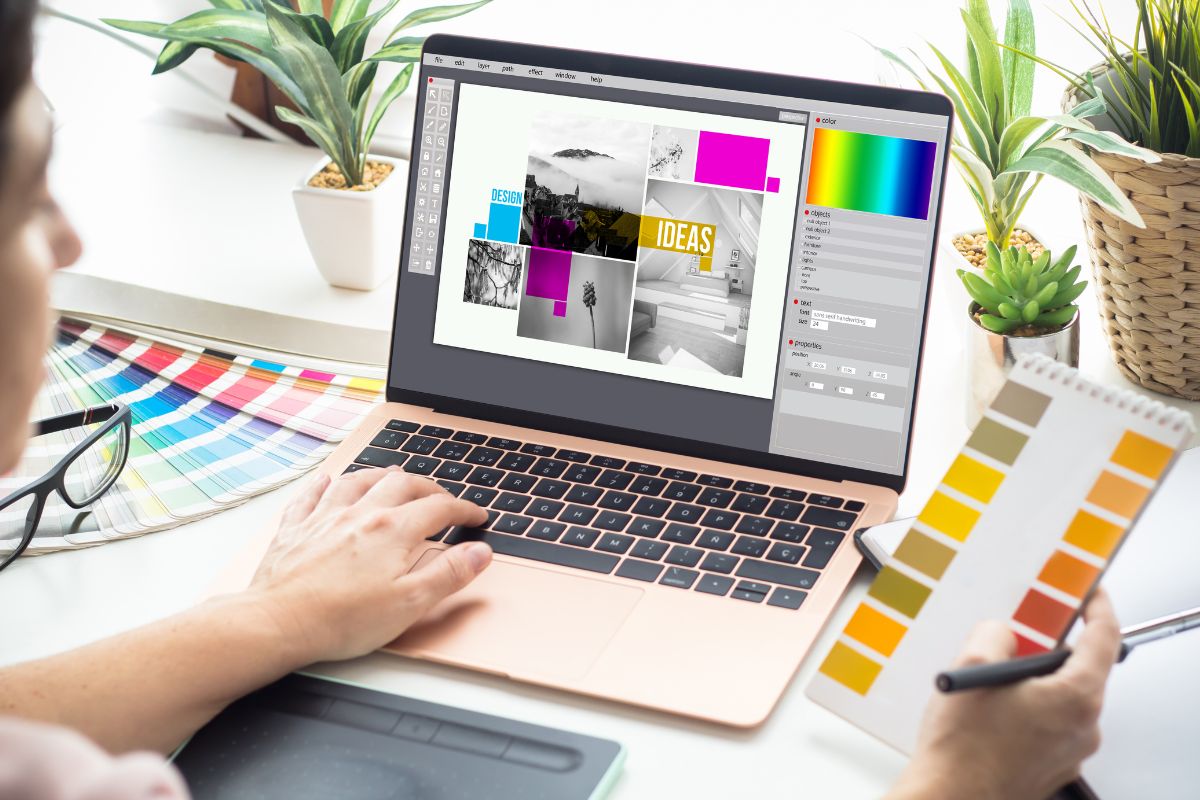 Graphic designer working on a laptop with a color swatch in hand, editing images for SEO in a photo collage, surrounded by creative tools and plants.