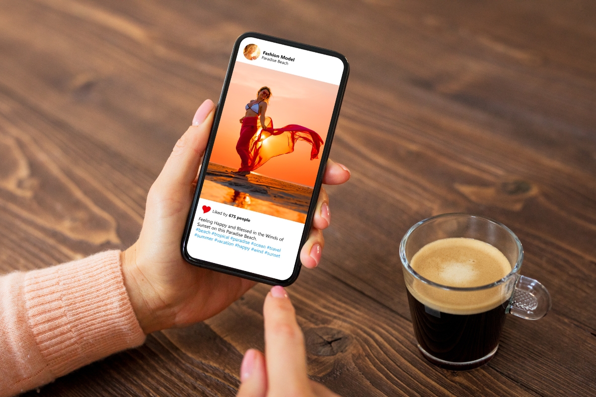 Hand holding a smartphone displaying an Instagram photo of a woman practicing yoga on a wooden pier at sunset, with a cup of coffee beside it on a table.