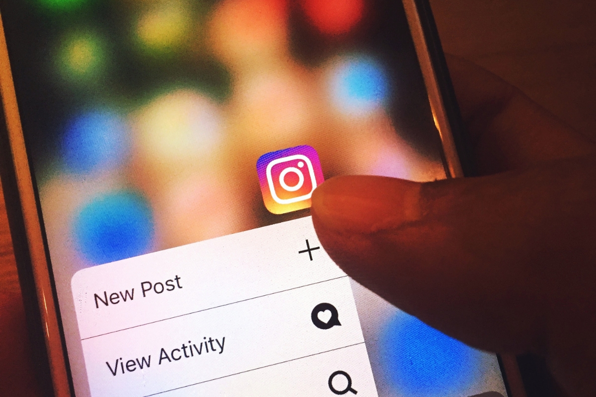 Person's finger about to tap the Instagram marketing tips app icon on a smartphone, with colorful blurred lights in the background.