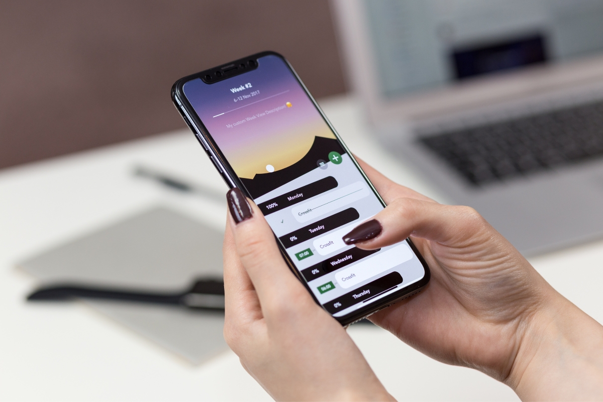 A person's hand holding a smartphone displaying an Instagram marketing tips app interface, with a laptop visible in the background.