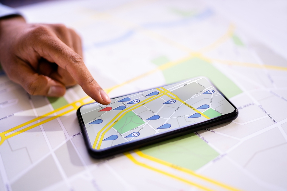 Person using a smartphone with a map application, displaying local business citations, placed on top of a paper map, indicating a location with their finger.