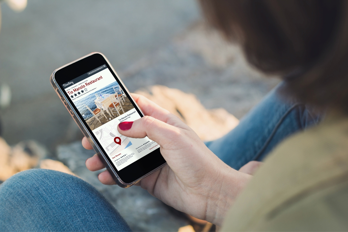 Woman using a smartphone with a map application displaying local business citations on the screen, sitting outdoors.