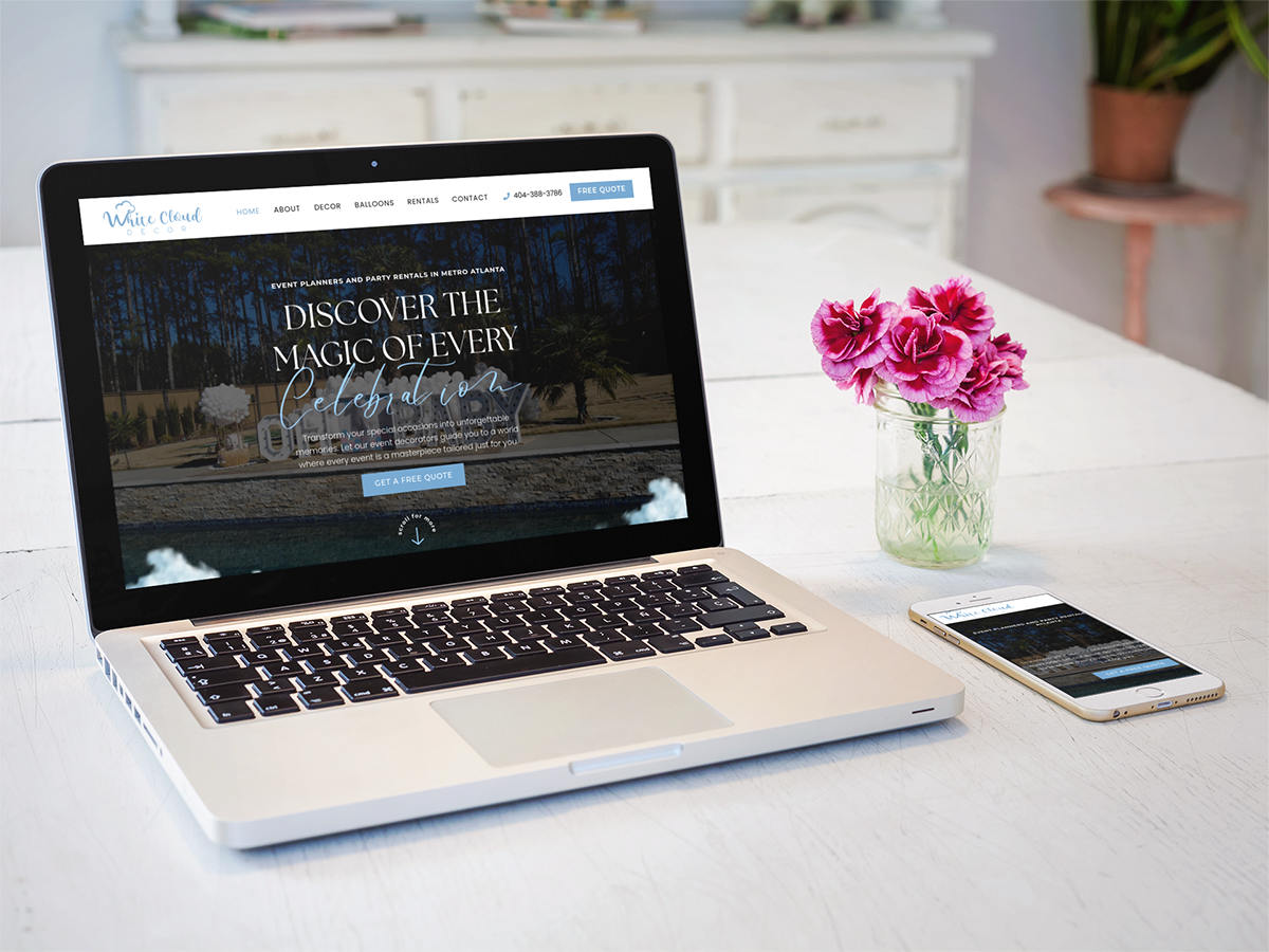 A laptop and a smartphone on a white desk displaying a travel website, with a vase of pink roses and white cloud decor beside them.