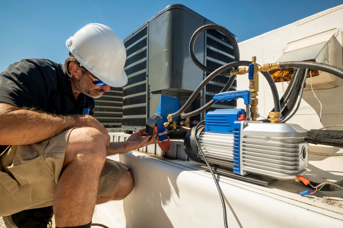 A technician in a white hard hat kneels while repairing an air conditioning unit on a rooftop under clear blue skies, ensuring the community's comfort—a prime example of effective community marketing.