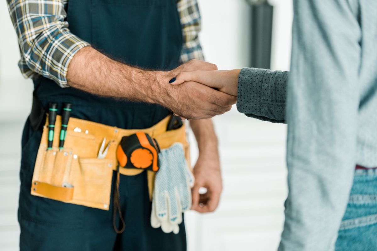 A worker wearing a tool belt shakes hands with another person, illustrating the essence of content marketing for plumbers.