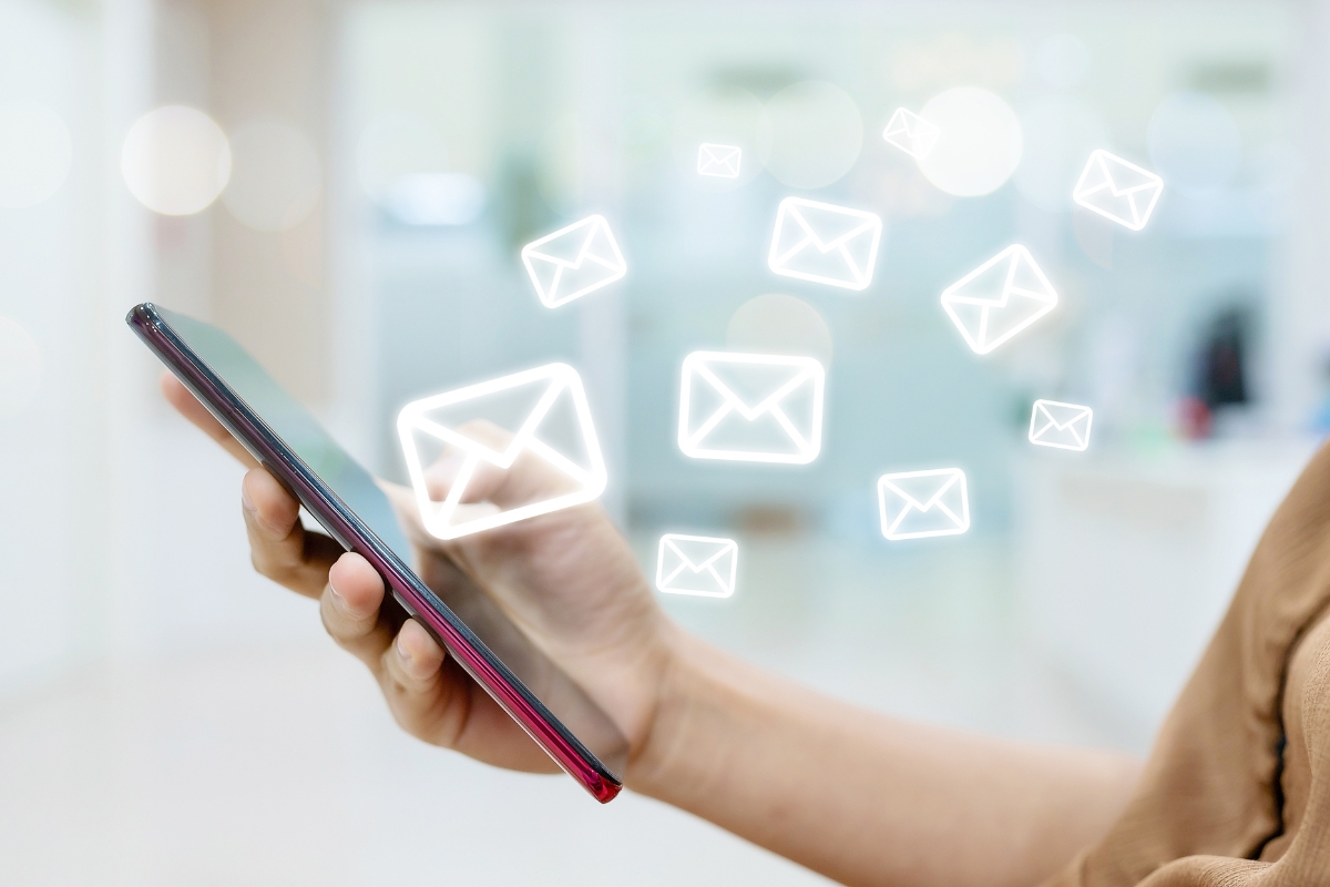 A person holds a smartphone with several envelope icons floating above, representing email messages being sent or received—showcasing the power of email marketing for plumbers.