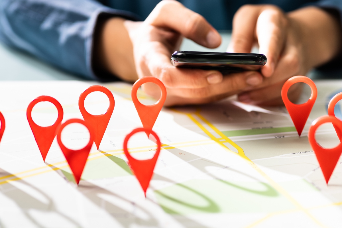 A person holds a smartphone over a map with several red location markers placed on it, likely examining the service area pages for key information.