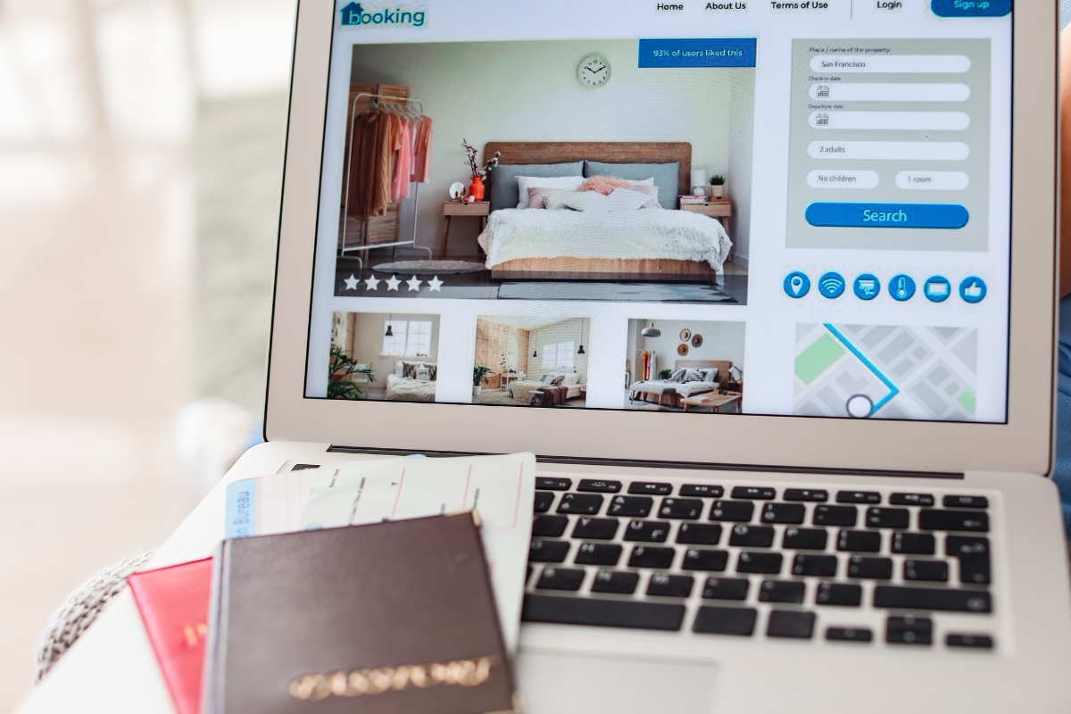 A laptop screen displays a hotel booking website with several rooms listed. Nearby, there are passports and a boarding pass on top of the laptop, suggesting an imminent trip planned through comprehensive service area pages.