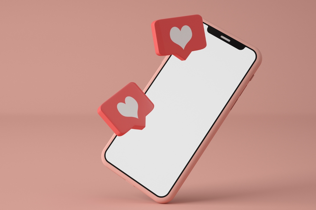 A smartphone displays two heart icons in speech bubbles, symbolizing likes or positive engagement from social media marketing for local businesses, against a peach-colored background.