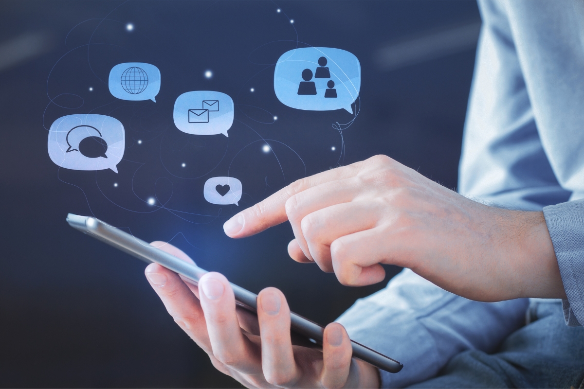 A person interacts with various digital icons on a smartphone screen, including a globe, chat bubbles, an envelope, a group of people, and a heart—tools essential for effective social media marketing for local businesses.