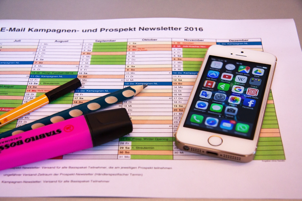 A colorful campaign schedule chart for the year 2016 is placed on a desk along with two pens, a highlighter, and a smartphone displaying various app icons on its screen—a perfect setup for laying out your social media marketing plan.