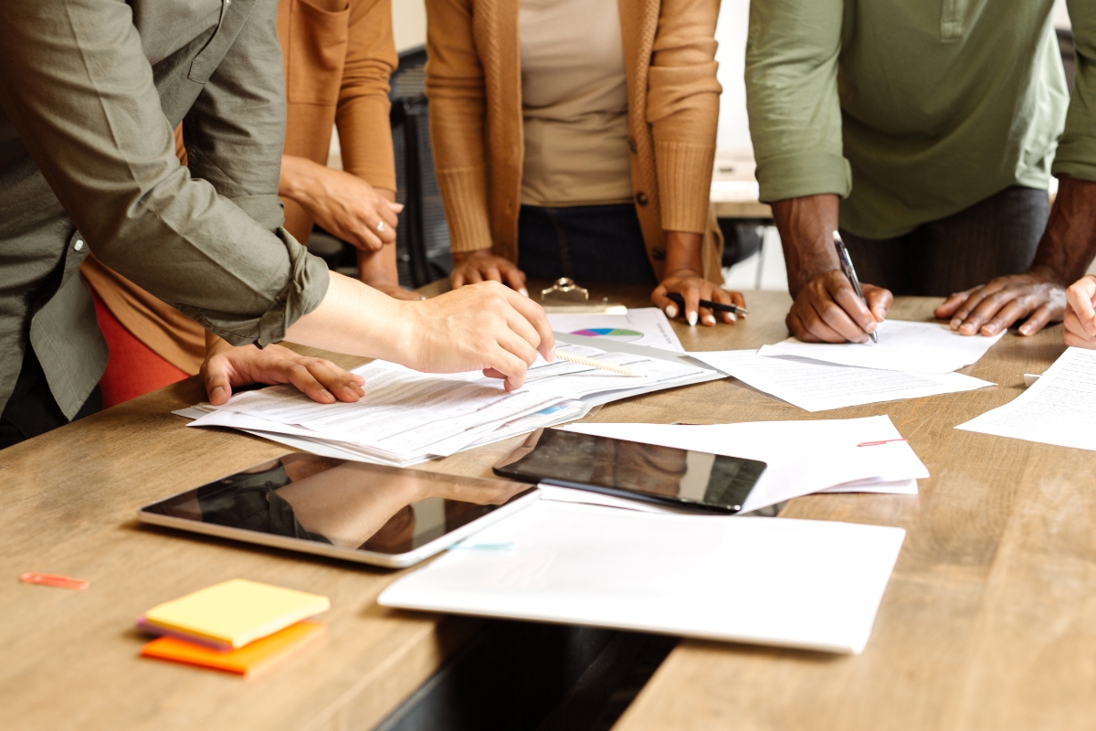 People gathered around a table with documents, pens, tablets, and sticky notes, engaging in a collaborative work session to develop a social media marketing plan.