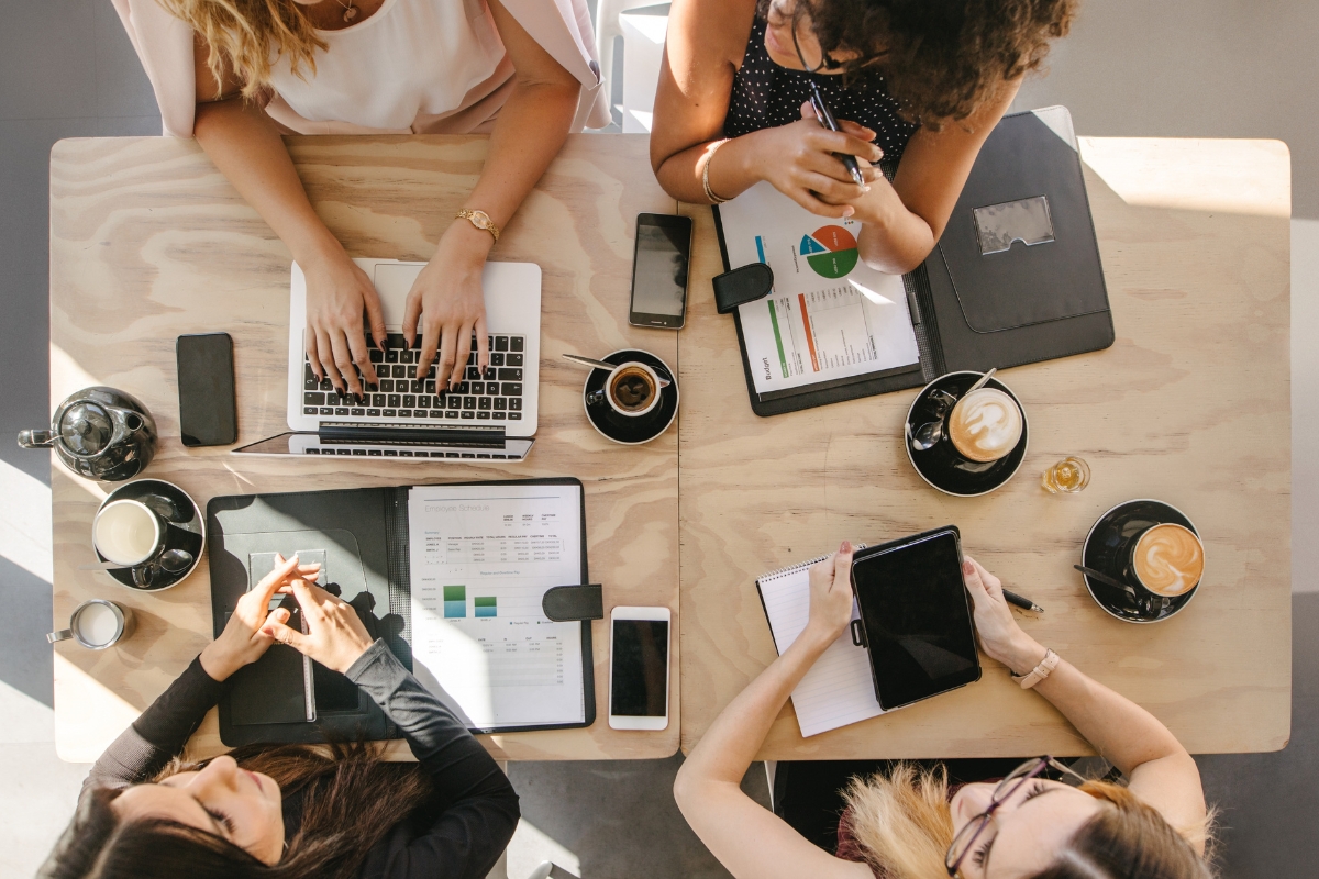 Four individuals sit around a table with laptops, tablets, smartphones, coffee cups, and documents, engaging in a collaborative work session. This scene unfolds in one of the best places to work remotely in Atlanta.