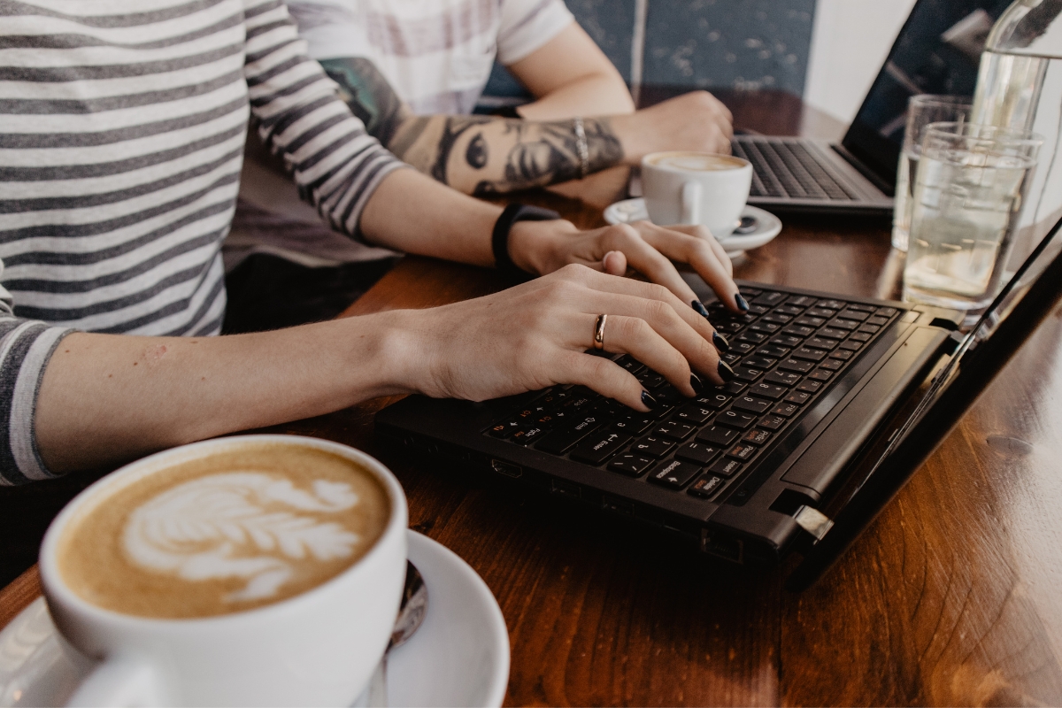 Two individuals working on laptops at a wooden table with two cups of latte, one person with a tattoo on their arm and wearing a smartwatch, exemplify the ambiance found at some of the best places to work remotely in Atlanta.