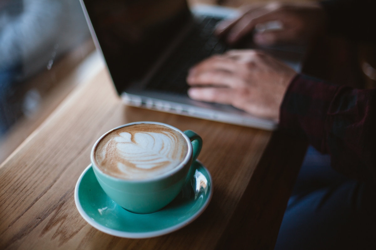 A person types on a laptop at a wooden table next to a teal cup of coffee with latte art, perhaps exploring the best places to work remotely in Atlanta.