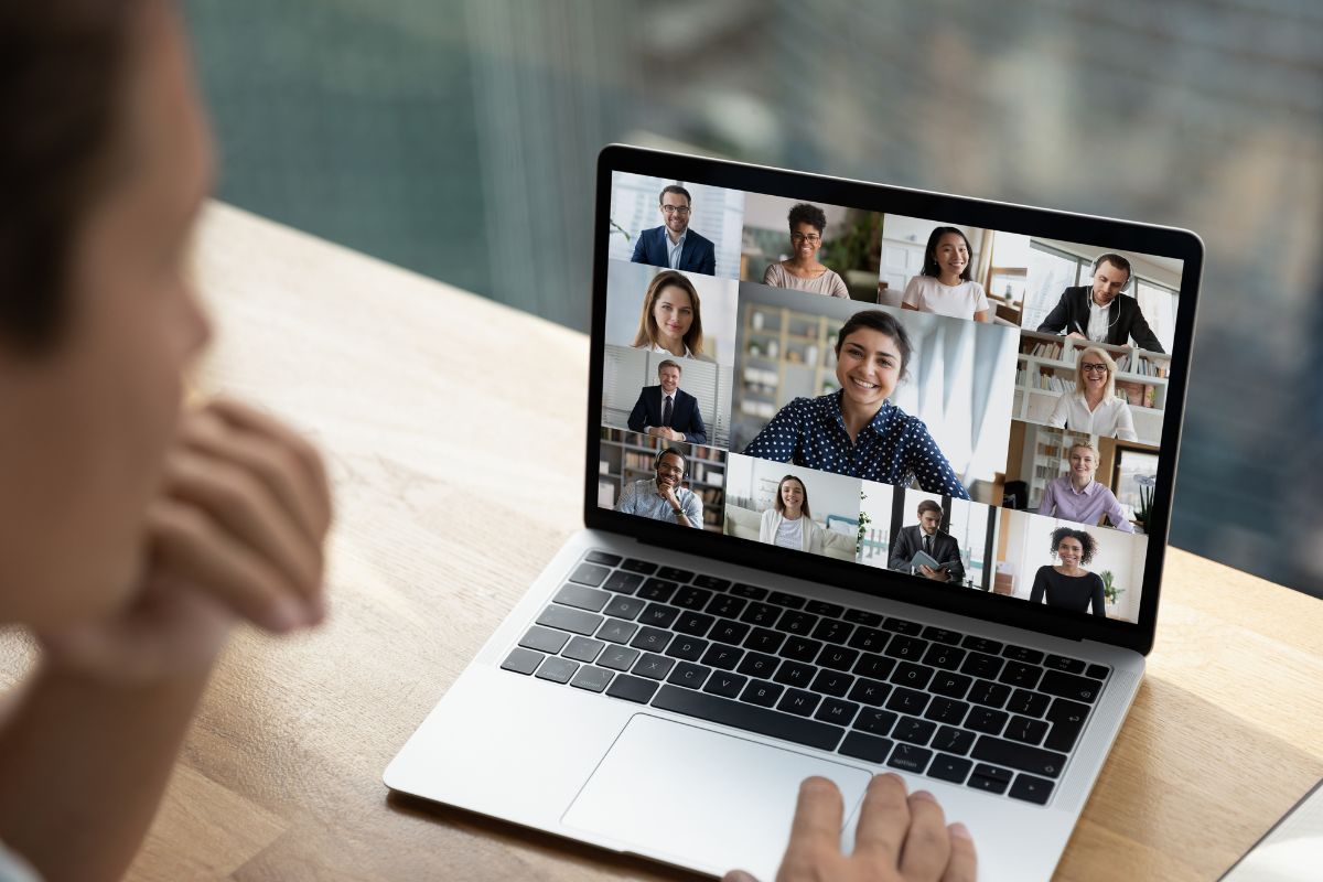 A person participates in a video conference with nine other individuals shown on a laptop screen, while sharing video testimonials to enhance the discussion.