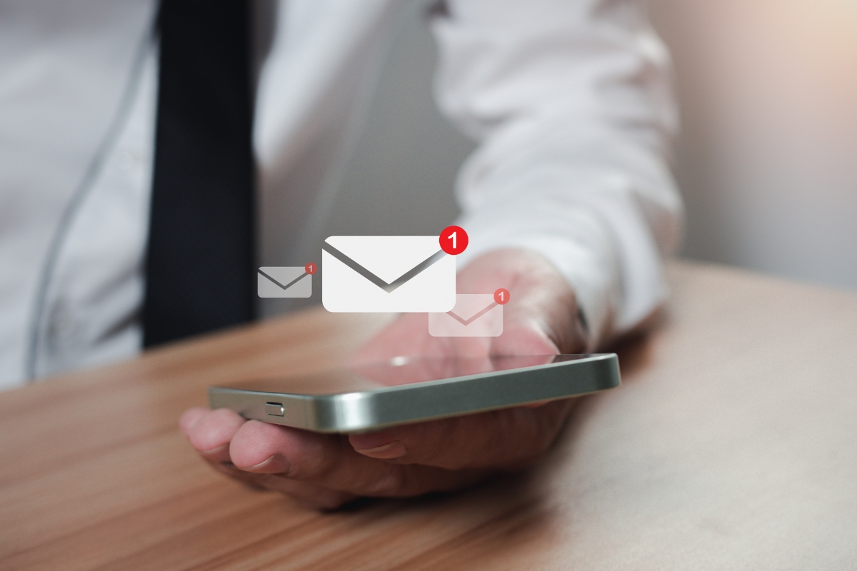 A person in formal attire holds a smartphone, where notifications for new email messages appear on the screen, highlighting the effectiveness of email targeting.