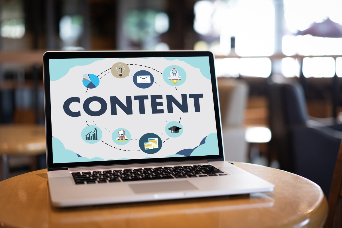 A laptop on a wooden table displays the word "CONTENT" on its screen, surrounded by various icons symbolizing how to write quality content, including an email, light bulb, rocket, graph, and graduation cap.