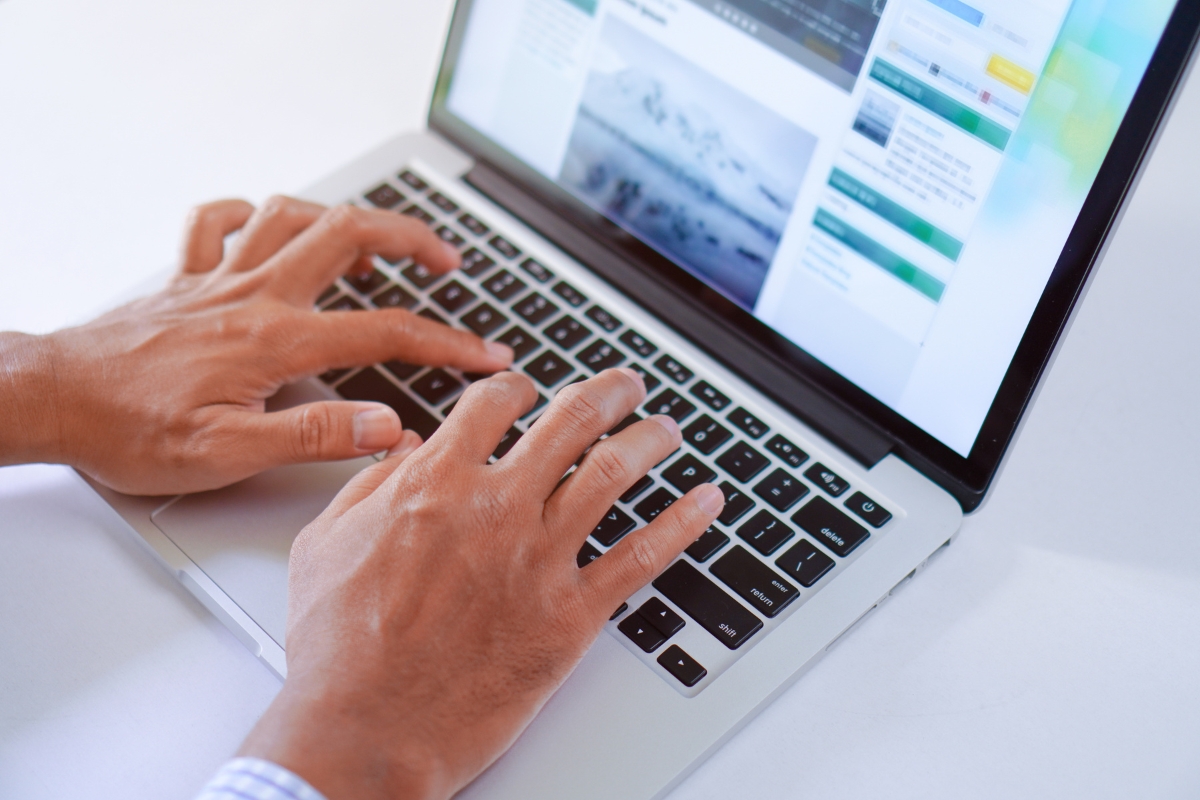 Two hands typing on a laptop keyboard, with a screen displaying a website containing images and text on how to write quality content.