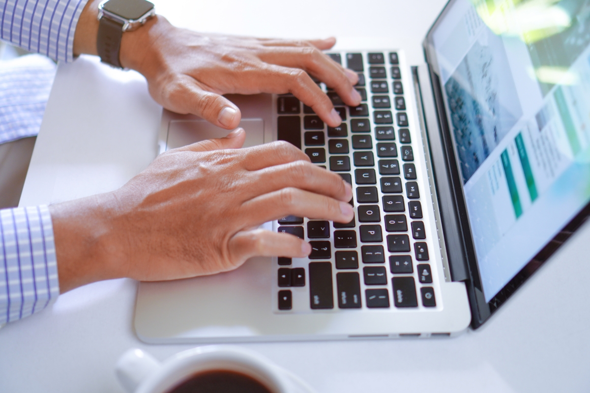 A person types on a laptop keyboard with a webpage open on the screen, likely exploring how to write quality content. A cup of coffee is placed nearby on a white surface.