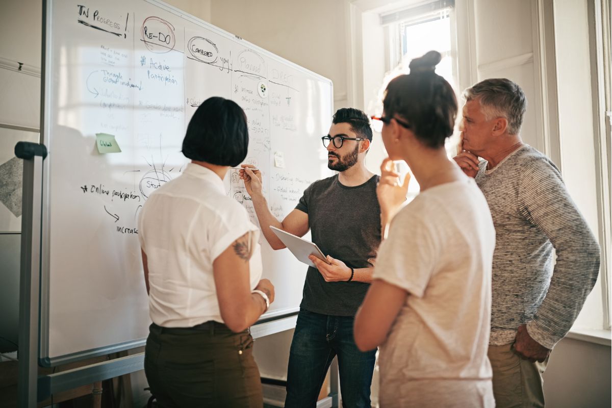 A group of four people stand around a whiteboard covered with notes, diagrams, and text, engaging in a collaborative discussion on what is semantic search.